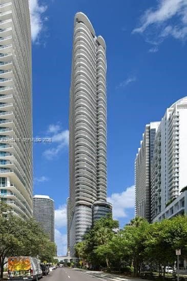 High-rise residential tower featuring a curvilinear glass facade, wrap-around balconies, and a structured concrete exterior