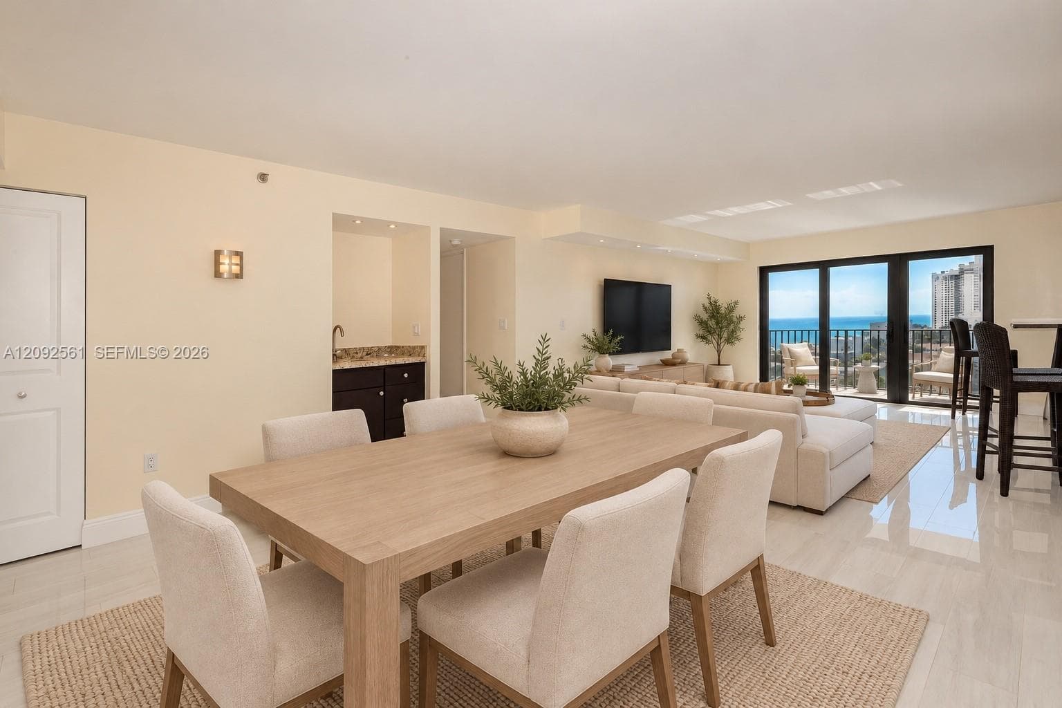 Open-concept living space featuring high-gloss tile flooring, built-in wet bar with stone countertop, and black-framed sliding glass doors opening to an exterior balcony