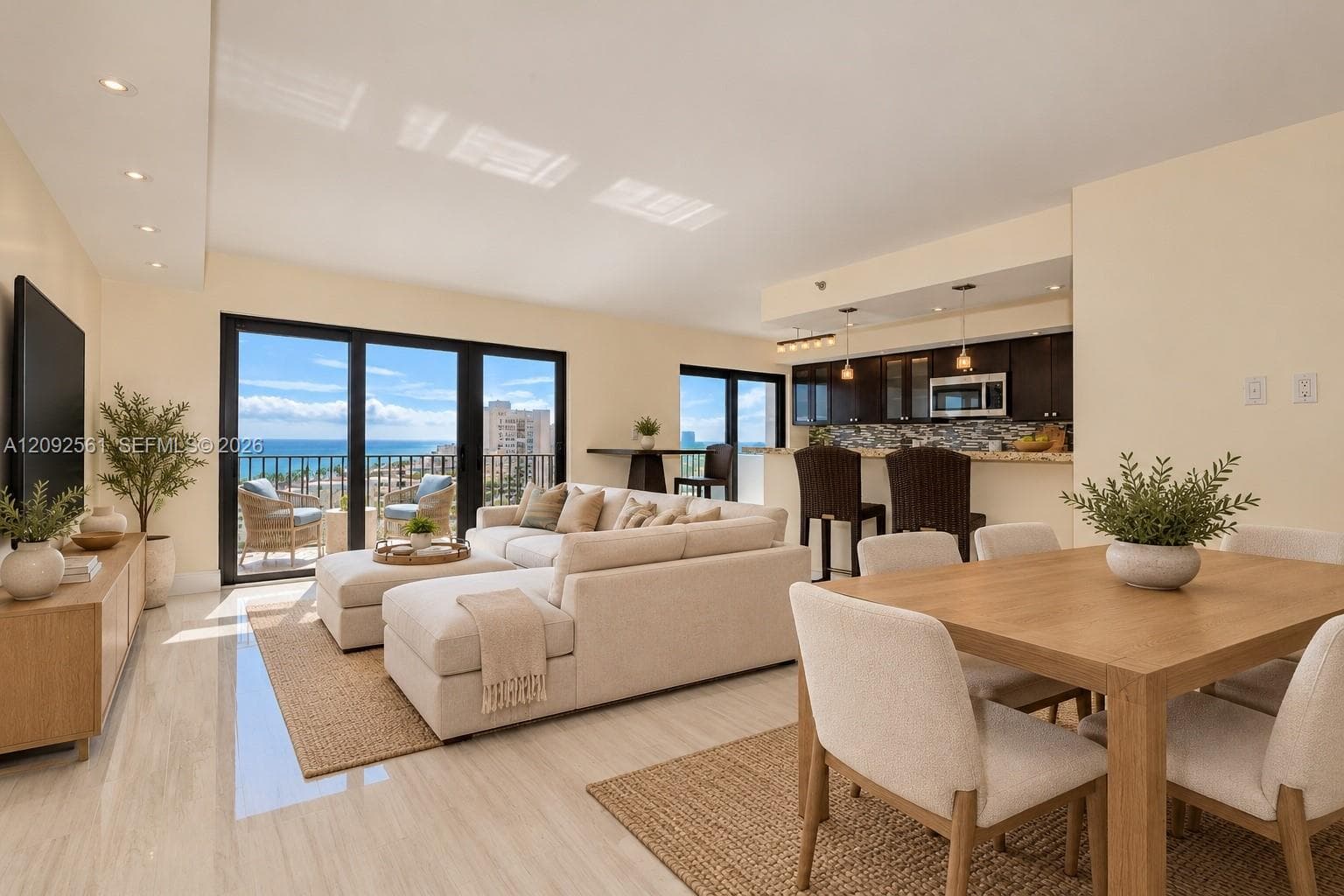 Open-concept living space featuring polished tile flooring, recessed lighting, dark wood-finish cabinetry, a tiled kitchen backsplash, and a balcony with an ocean backdrop
