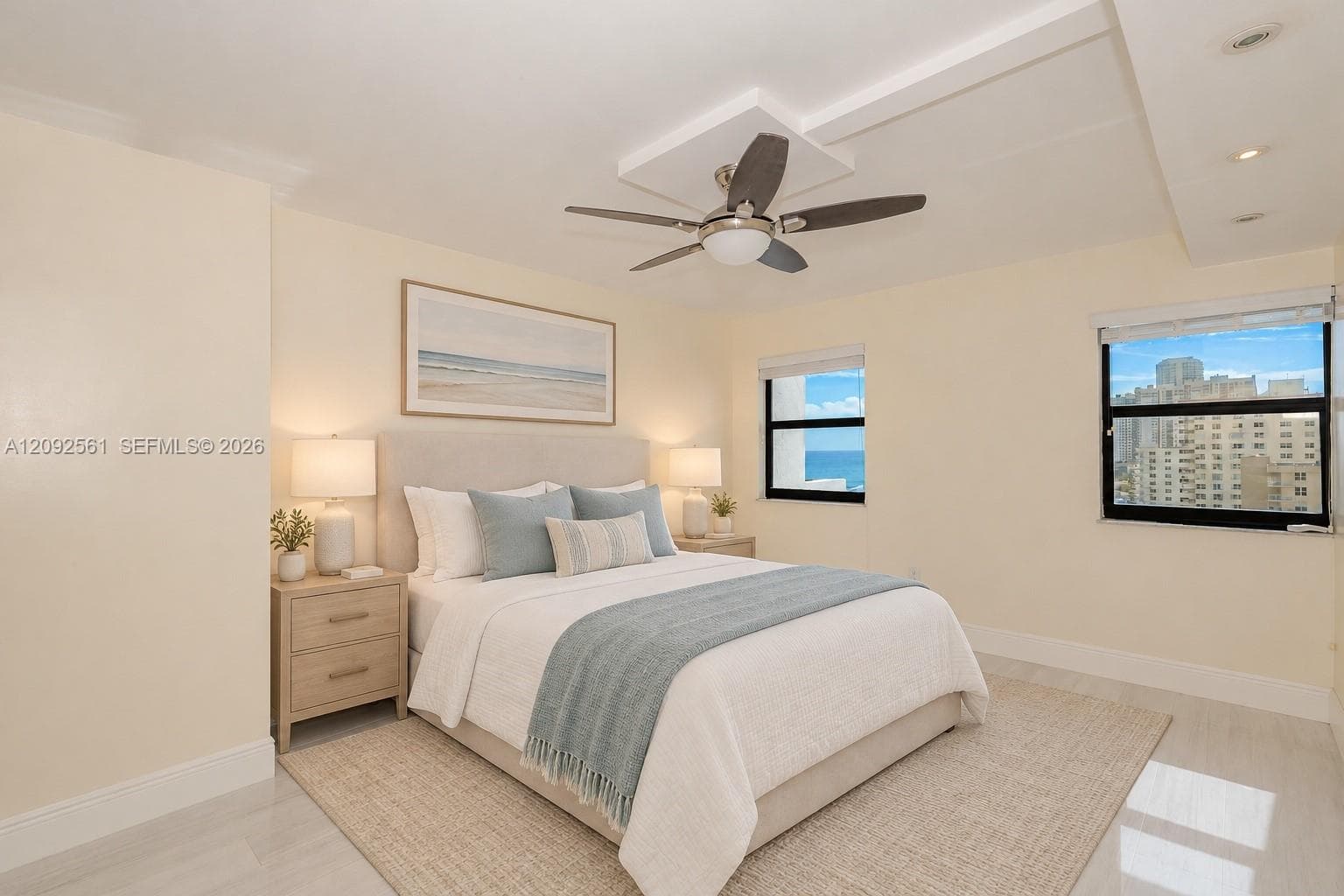 Neutral interior with light-toned flooring, recessed ceiling lighting, a central ceiling fan with integrated light, and windows showcasing ocean and coastal scenery
