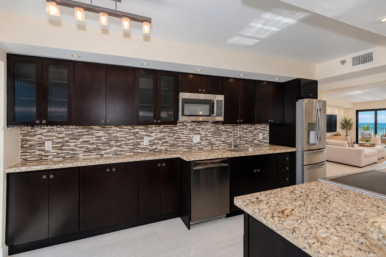 Kitchen featuring dark cabinetry, stone countertops, multi-tonal mosaic tile backsplash, stainless steel appliances, and a linear pendant light fixture