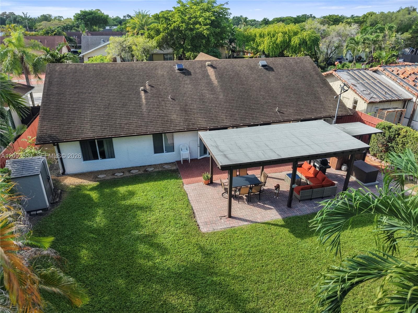 Expansive backyard featuring a manicured lawn, a large patio with a covered pergola, and a storage shed