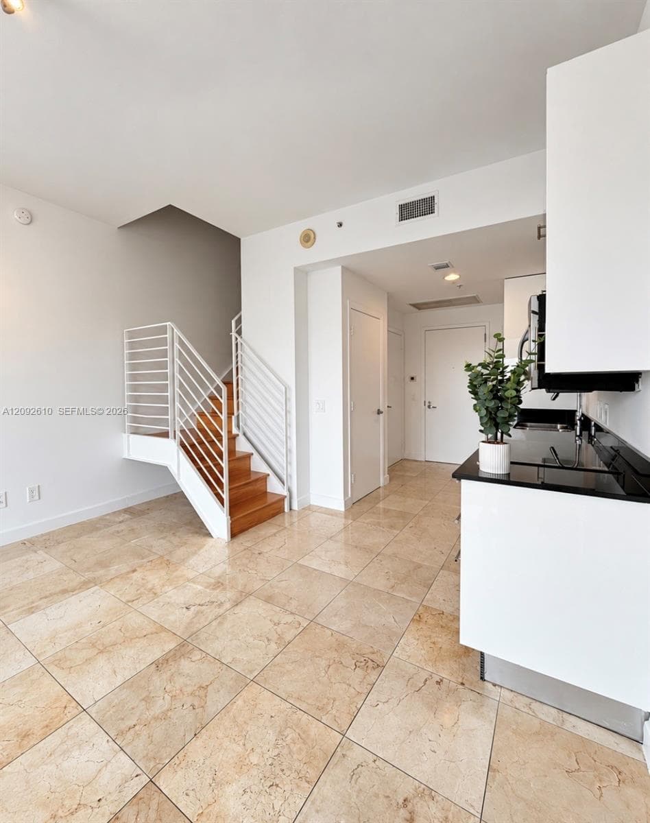 Polished stone tile flooring, open-tread staircase with white metal railings, white cabinetry, and dark-toned countertops