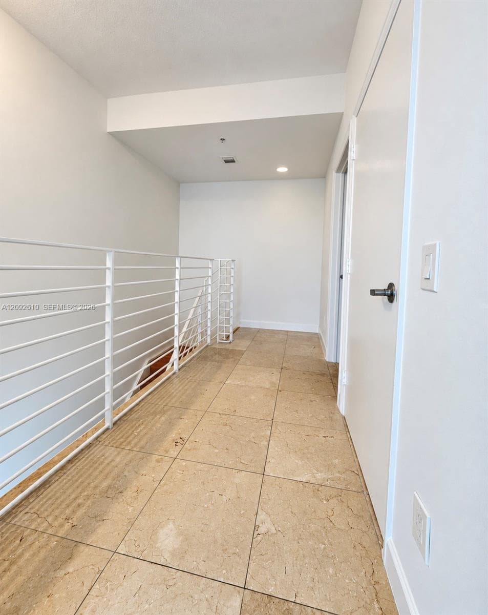 Hallway featuring oversized stone-finish floor tiles, white metal horizontal-rail banister, recessed lighting, and crisp white interior paint