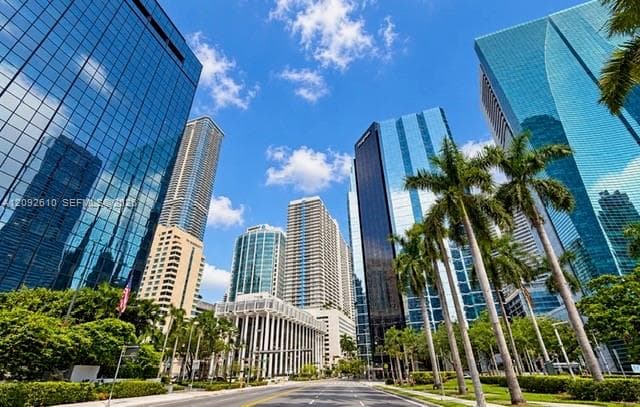Urban streetscape featuring high-rise glass-facade towers, manicured palm tree landscaping, and paved thoroughfare