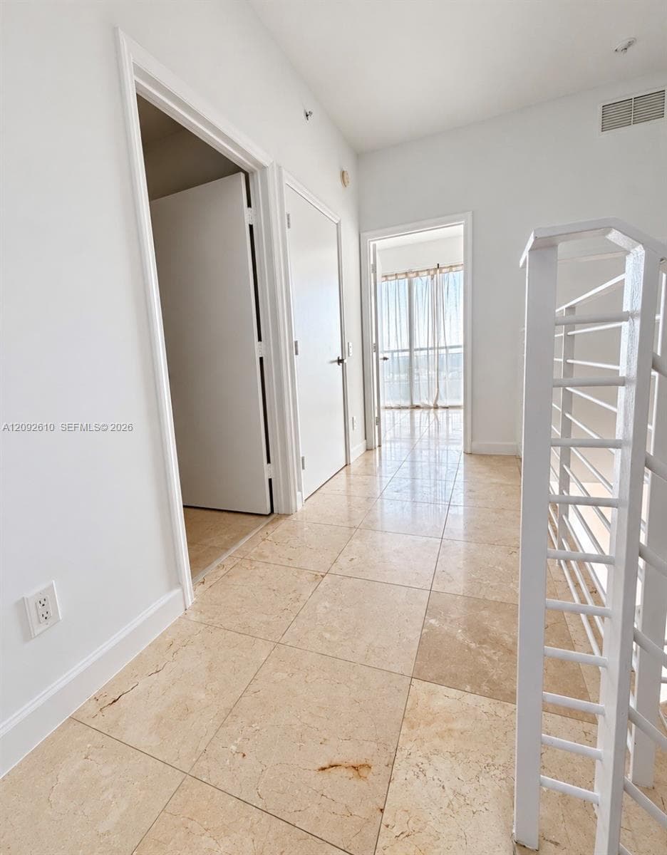 Hallway featuring large-format tile flooring, white shaker-style interior doors, and a white metal staircase railing