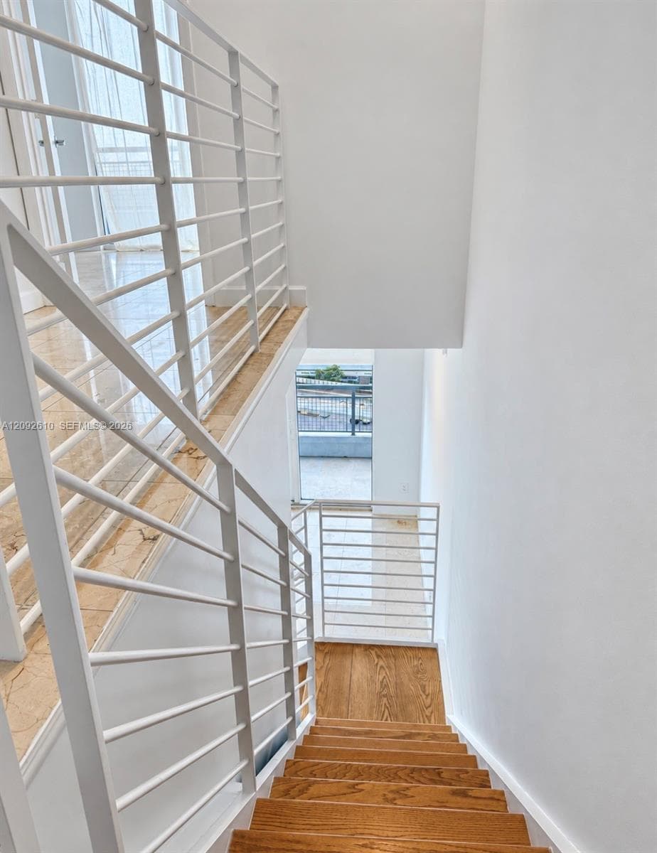 Staircase featuring wood-finish treads, white horizontal metal railings, and natural stone flooring on the landing