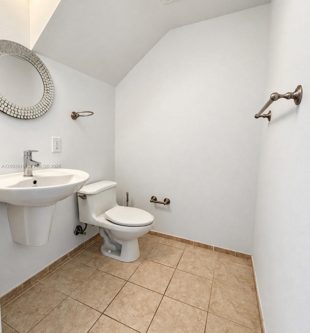 Wall-mounted pedestal sink, two-piece toilet, ceramic tile flooring, and metallic hardware finish