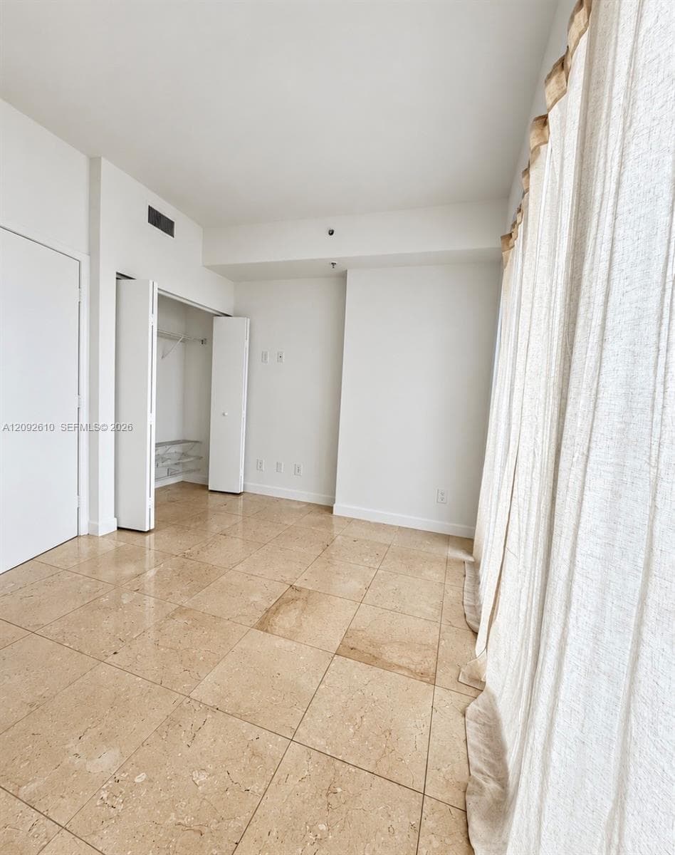 Polished stone flooring, walk-in closet with built-in shelving, and floor-to-ceiling windows