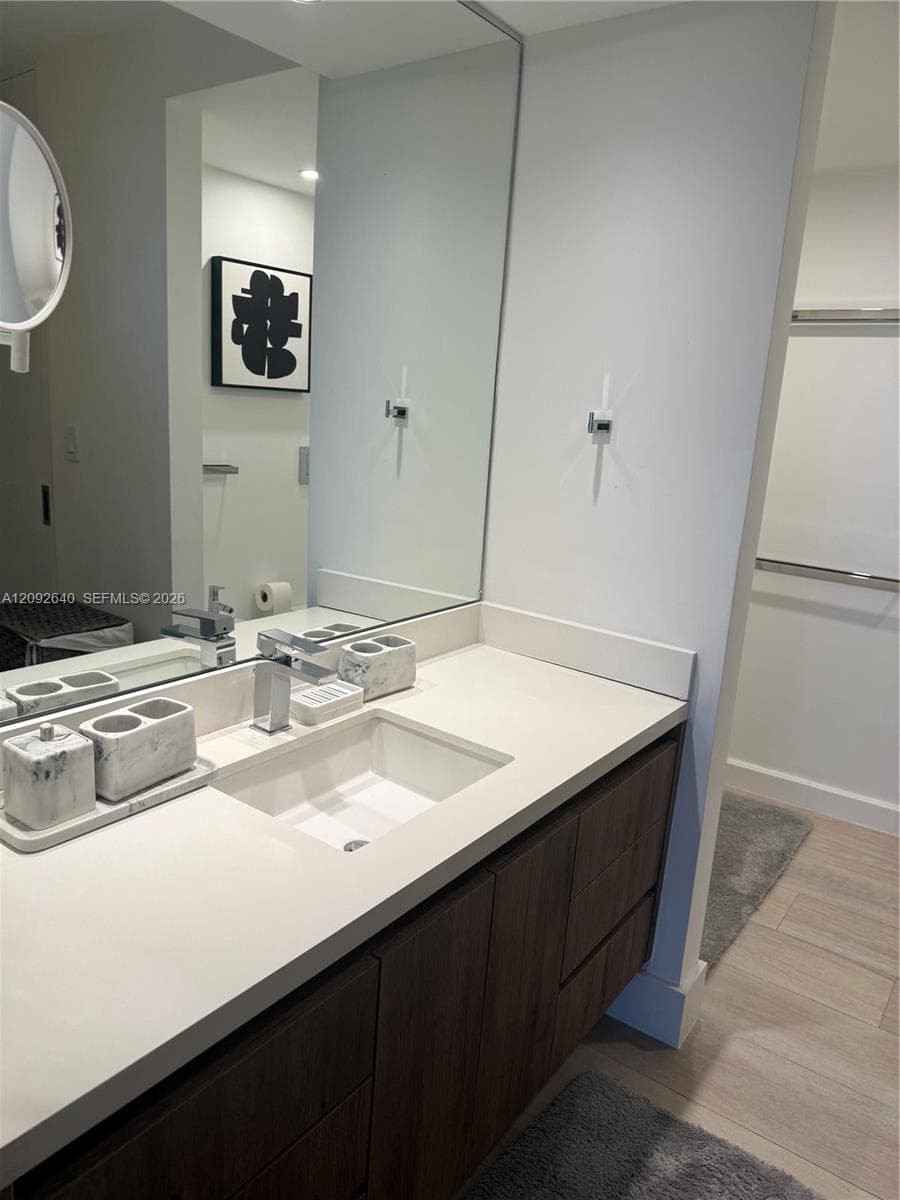 Modern vanity featuring wood-finish cabinetry, a white countertop with an integrated rectangular sink, a wall-to-wall mirror, and a chrome single-lever faucet