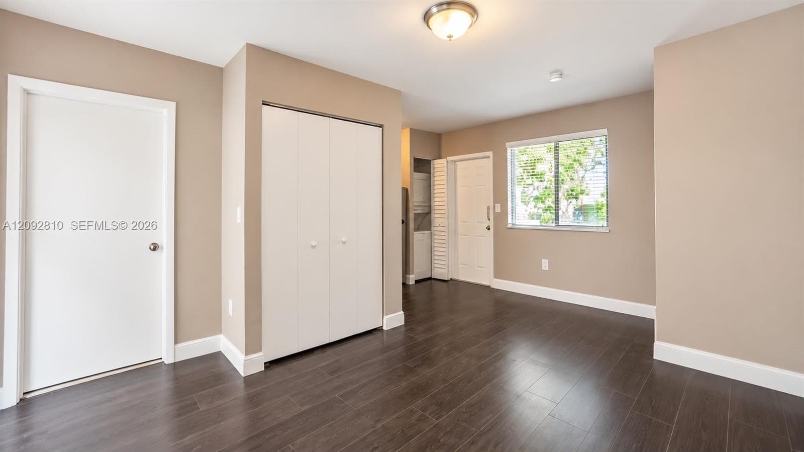 Interior space featuring wood-finish flooring, neutral wall paint, bi-fold closet doors, a single-hung window, and a flush-mount ceiling light fixture