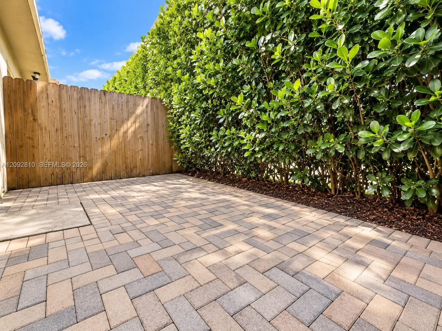Outdoor patio featuring multi-tone paver flooring in a herringbone pattern, wood-style privacy fencing, and mature hedge landscaping