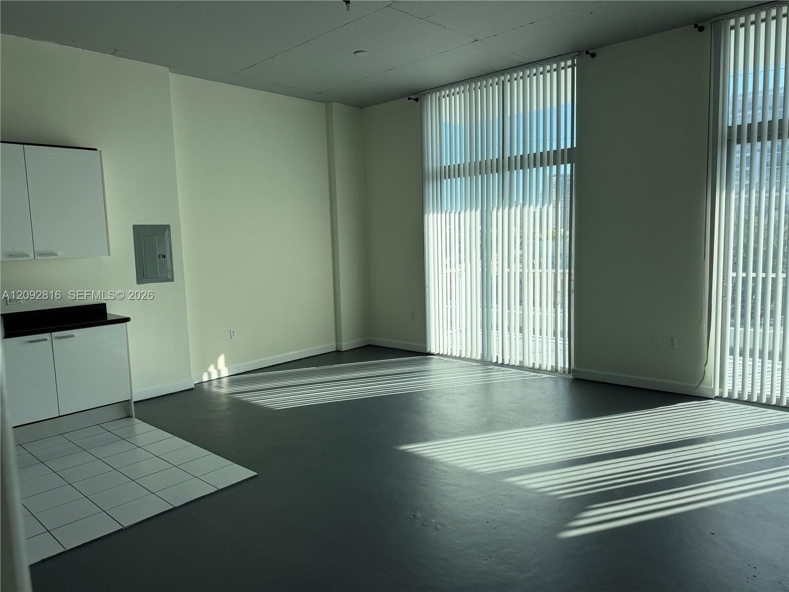 Expansive room with high ceilings, multiple tall windows with vertical blinds, and a built-in cabinetry unit with a dark countertop