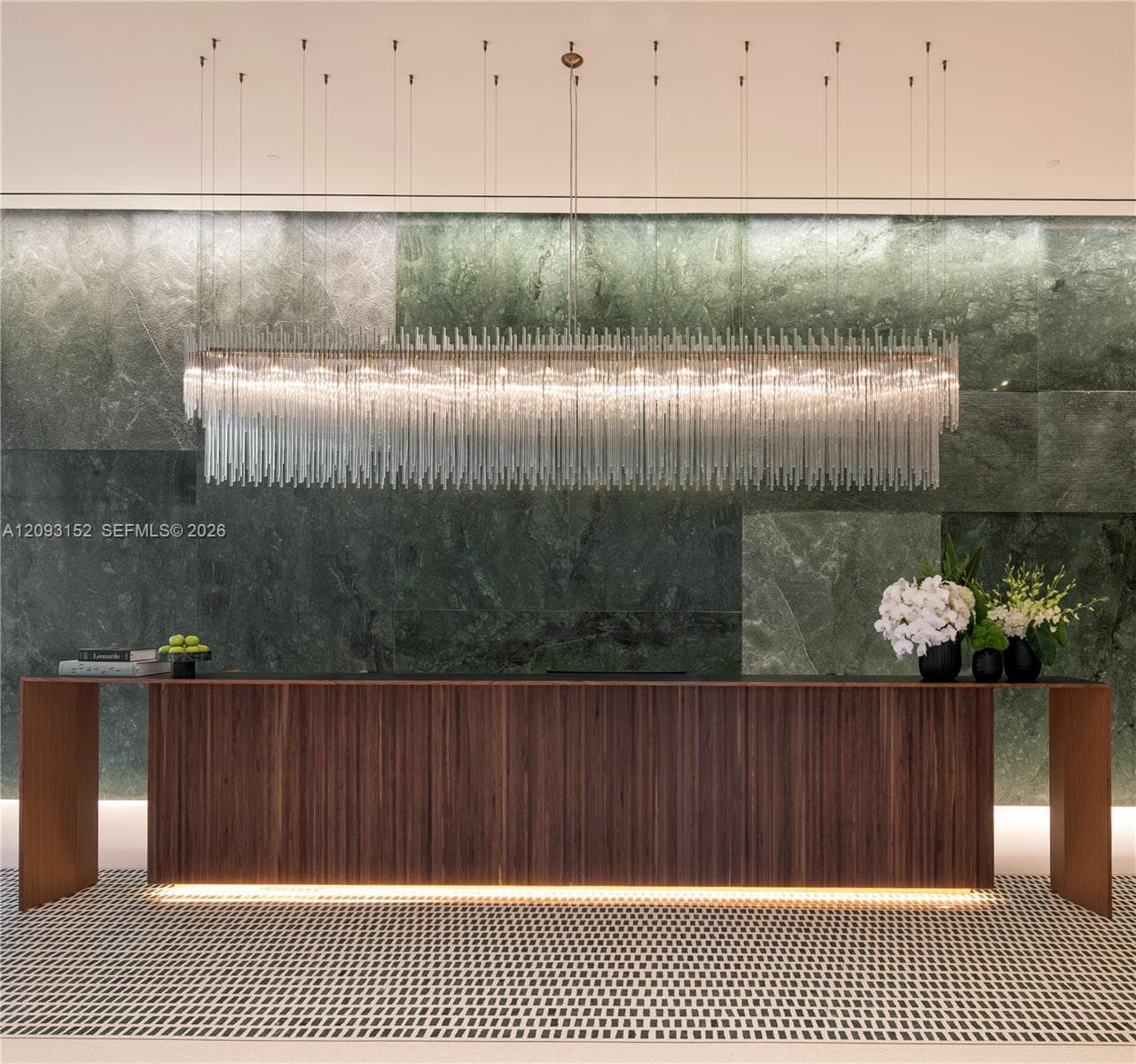 Large-scale green stone tile feature wall, custom linear multi-tiered crystal pendant light fixture, built-in wooden console with integrated base lighting, and patterned flooring