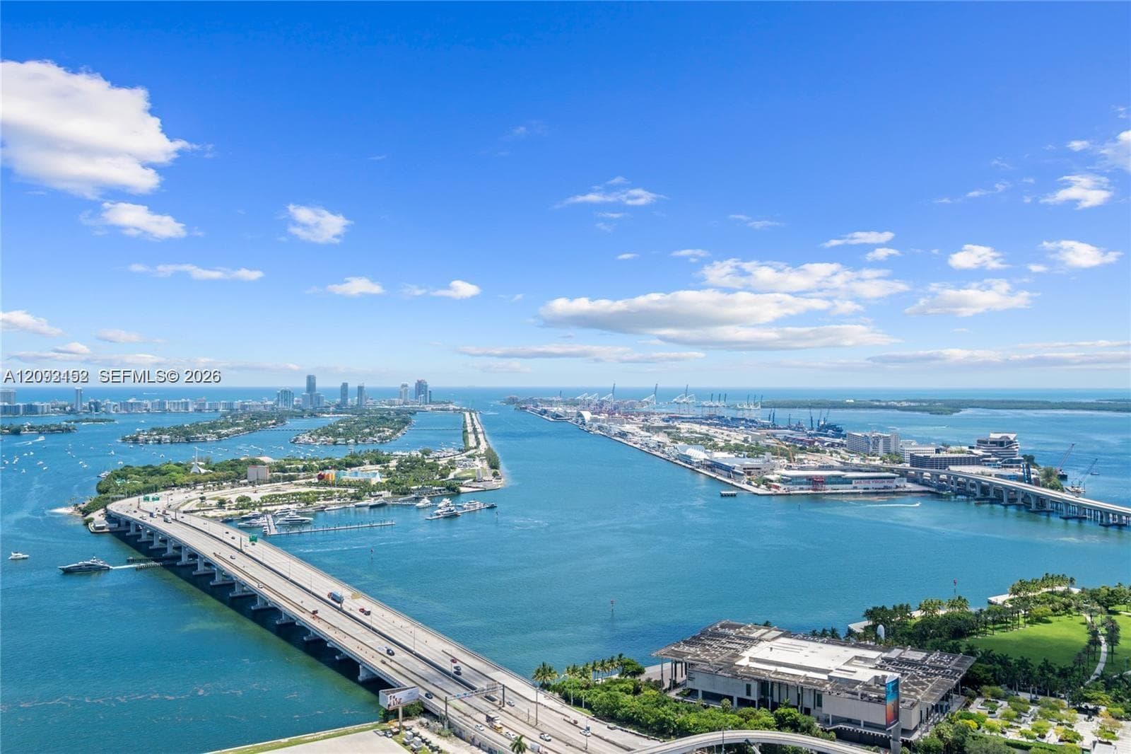 Panoramic coastal expanse featuring bridge infrastructure, maritime waterways, distant high-rise urban skyline, and sprawling parkland