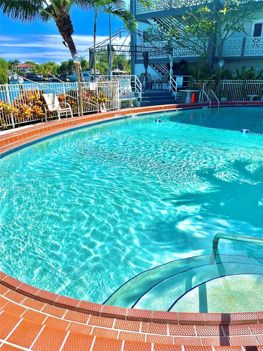 Curved swimming pool with brick coping, integrated steps, and surrounding white perimeter fencing