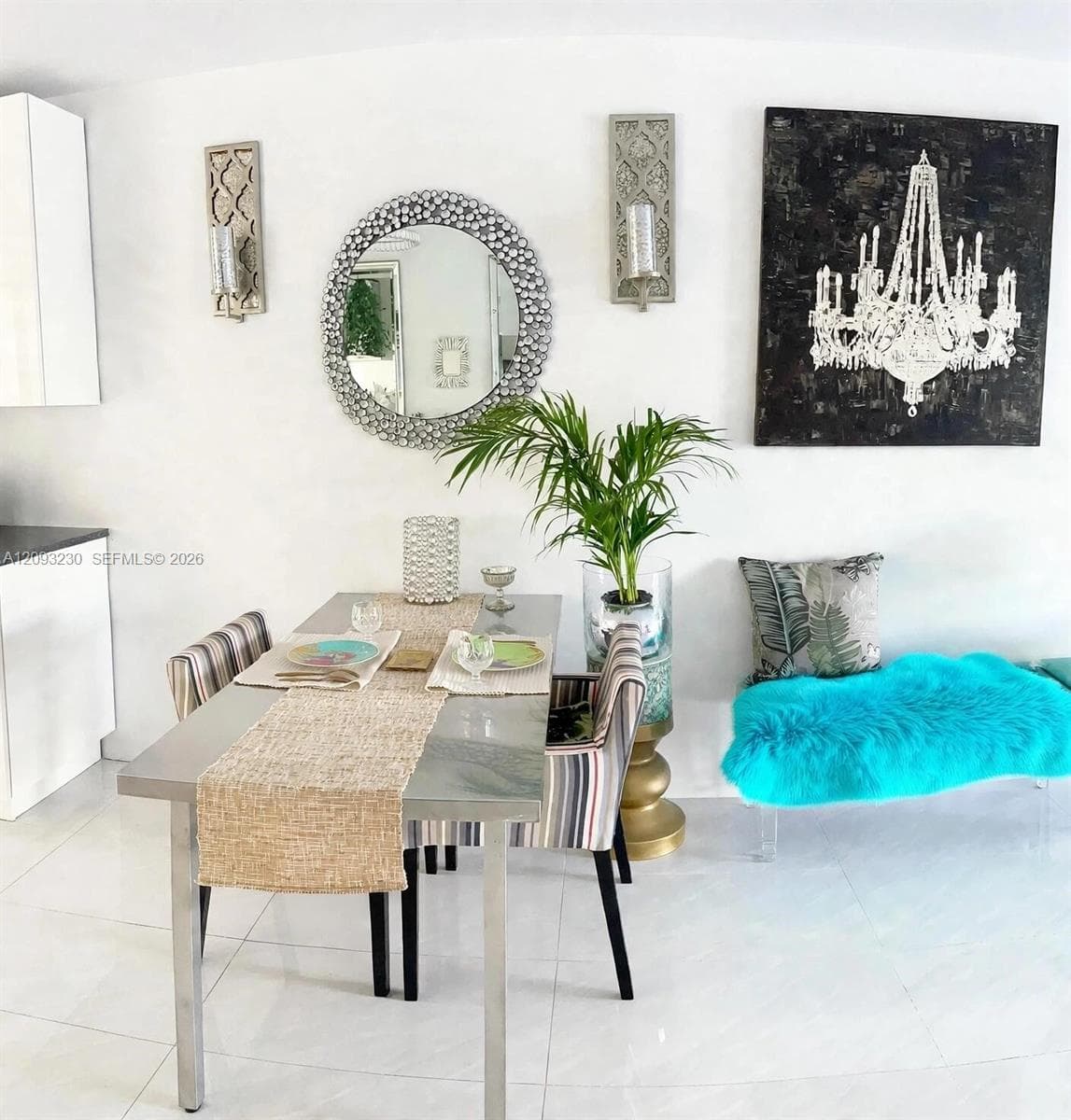 White tile flooring, wall-mounted decorative sconces, a circular mirror with an embellished frame, and white cabinetry with dark countertops