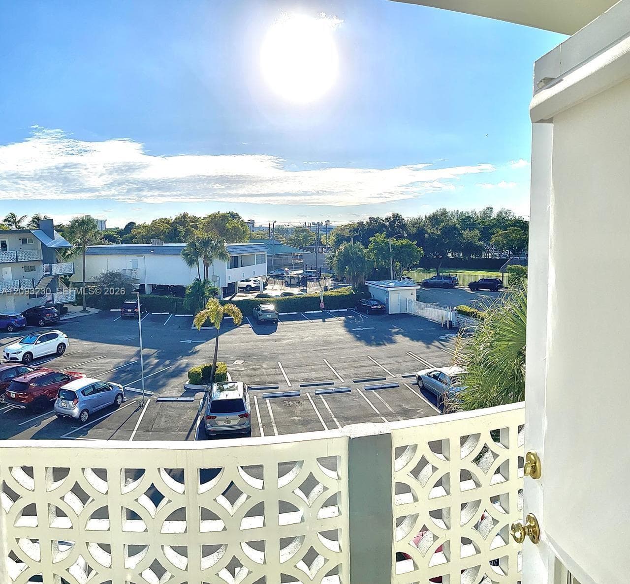 Outdoor balcony with an ornate decorative railing, overlooking a paved parking area and distant buildings