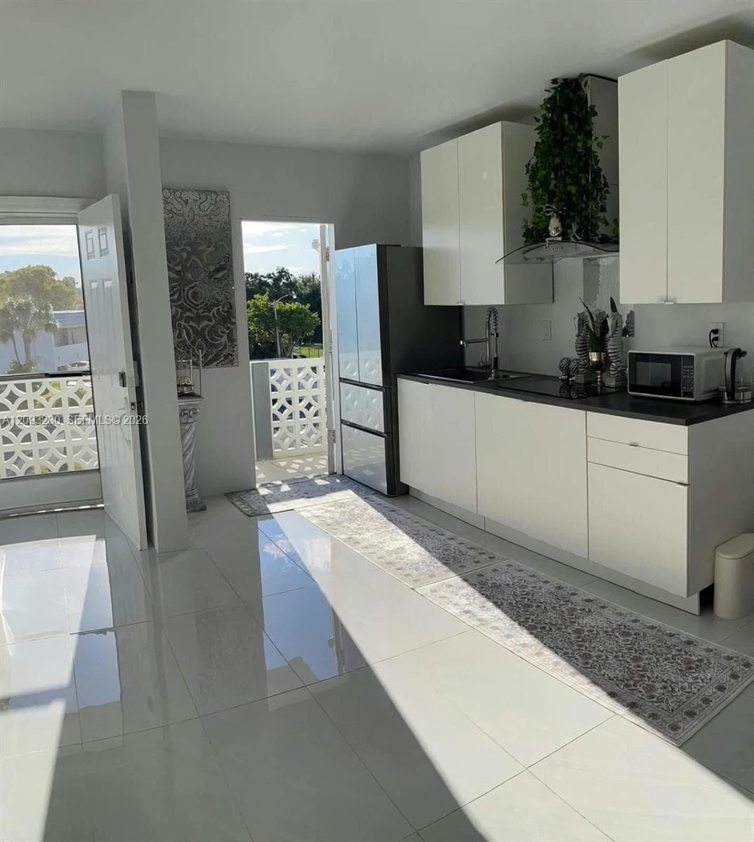 Kitchen featuring white flat-panel cabinetry, dark countertops, and a stainless steel range hood