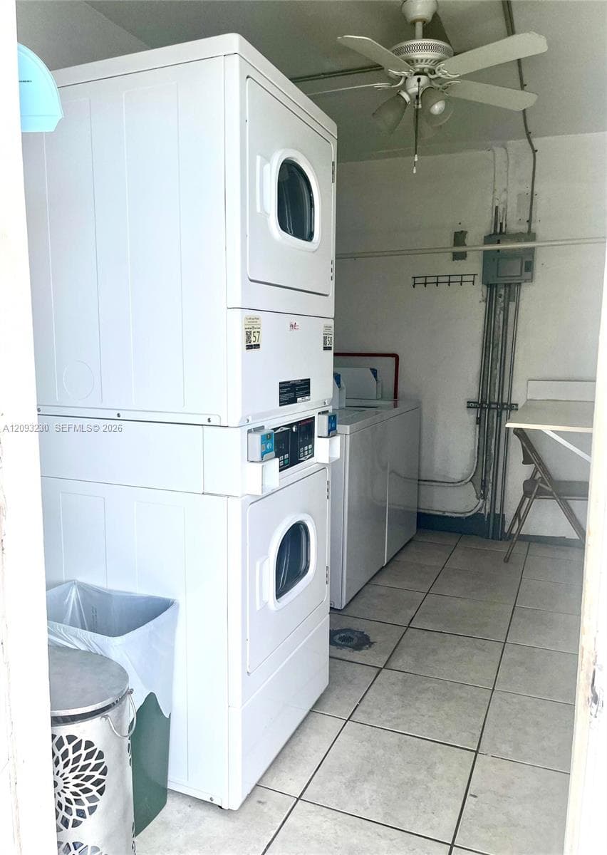 Laundry facility featuring tiled flooring, ceiling fan, stacked washer and dryer, and additional washer