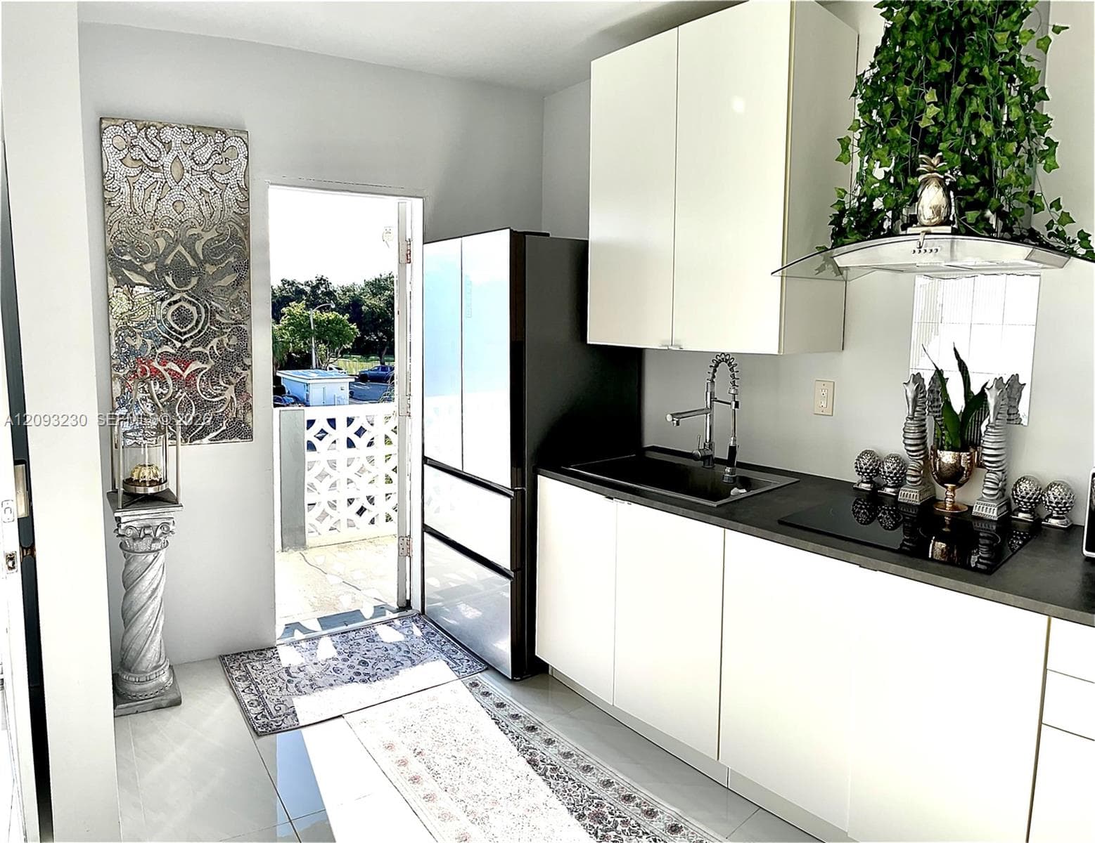 Sleek kitchen featuring white cabinetry, a dark countertop, an integrated sink, an induction cooktop, and a modern range hood