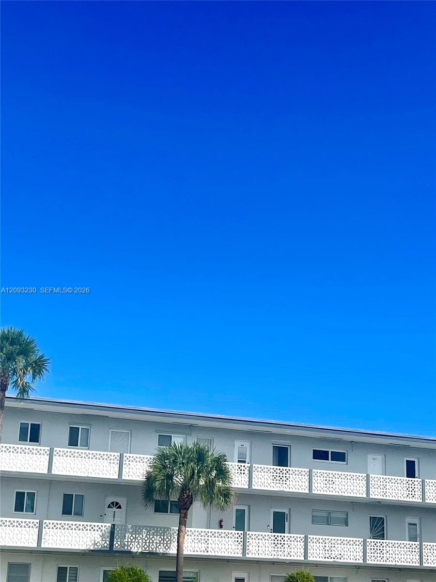 Multi-story building featuring white exterior, private balconies with decorative white railings, and mature palm trees