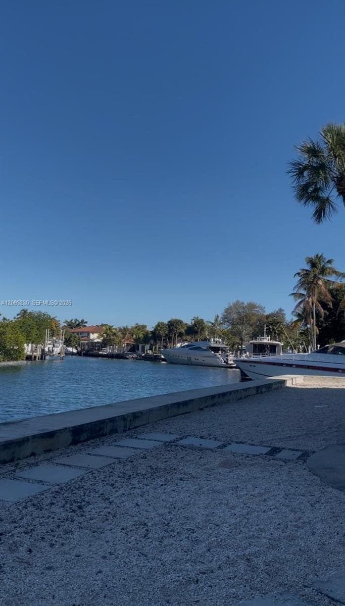 Waterfront setting with a concrete retaining wall, stone paver patio, and mature palm trees