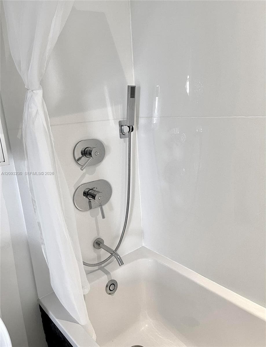 Bathtub with chrome fixtures, a hand shower, and white tile surround