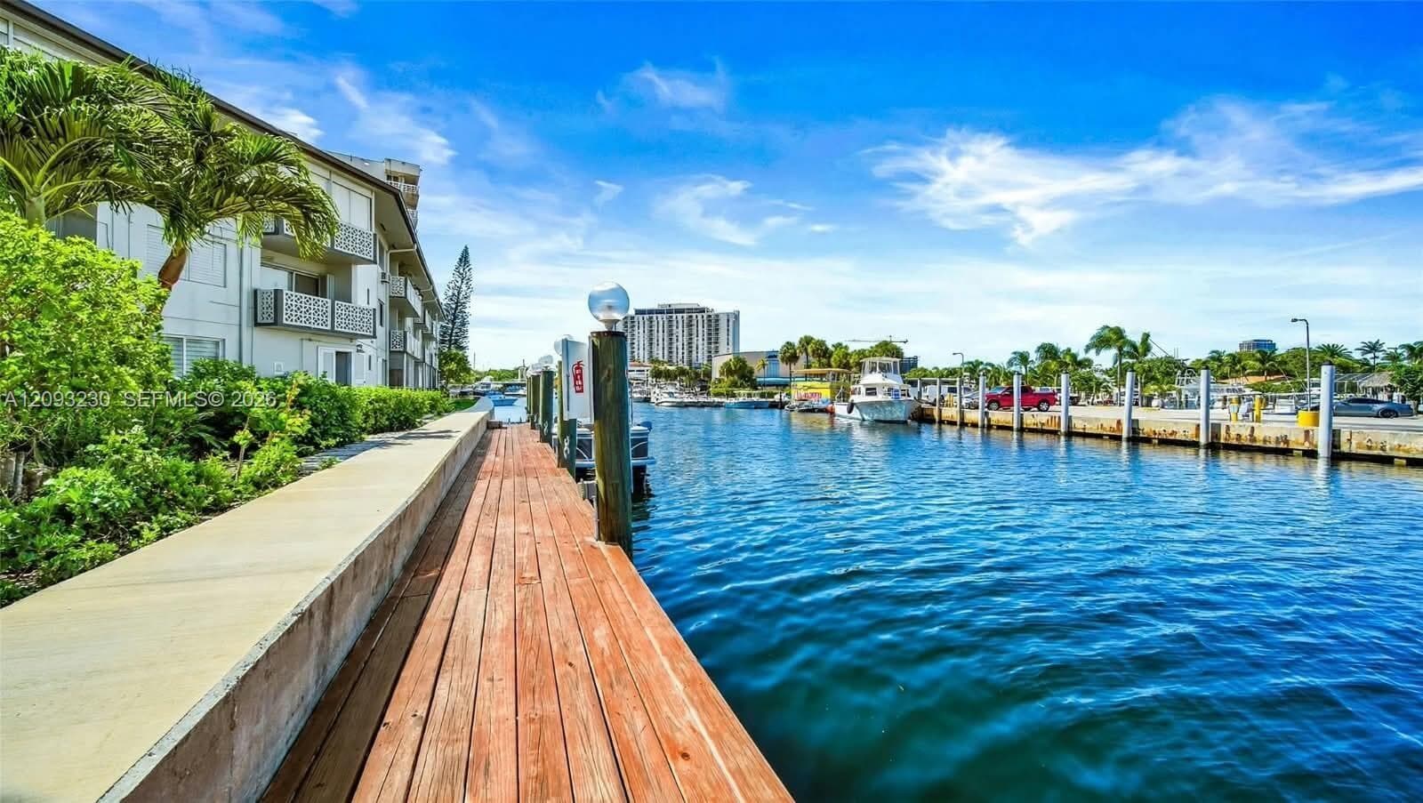 Waterfront property featuring a private wood dock, concrete walkway, and lush landscaping