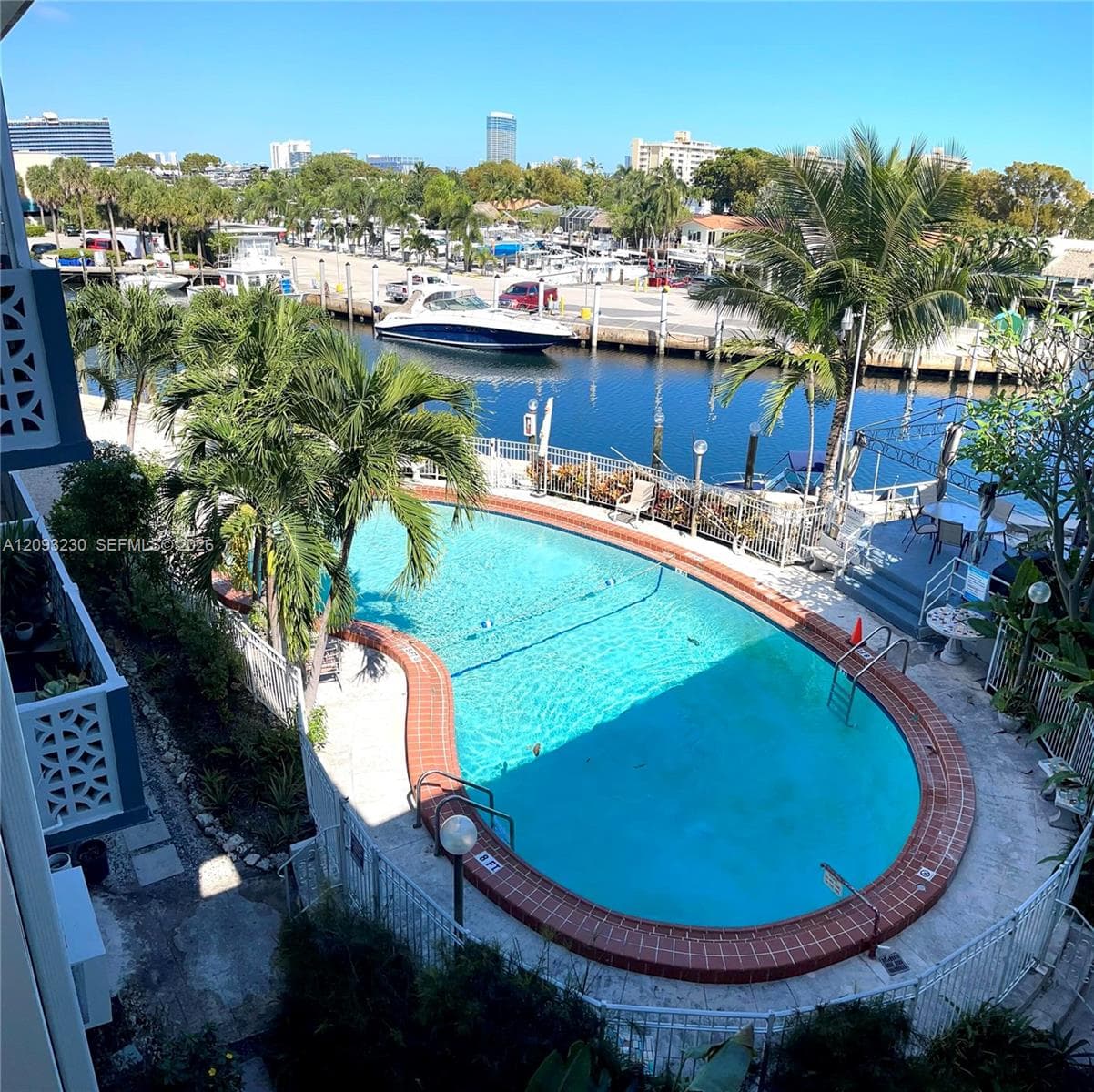 Curved swimming pool with brick coping, adjacent to a waterway with boat slips and a distant cityscape