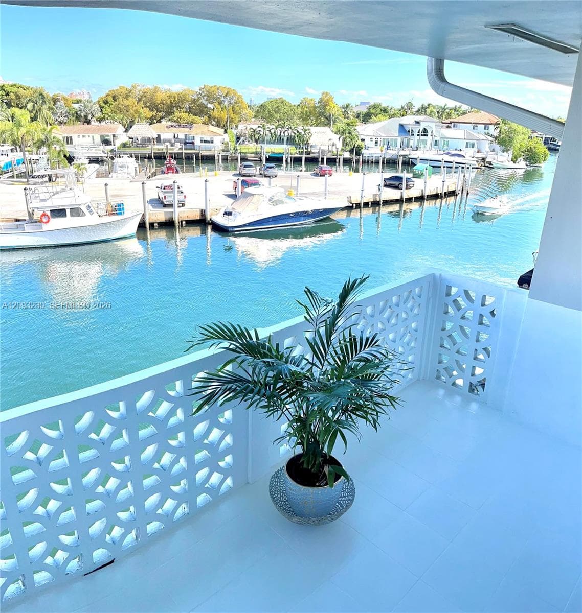 Balcony with white tile flooring and decorative patterned railing overlooking a waterway with boats and distant homes