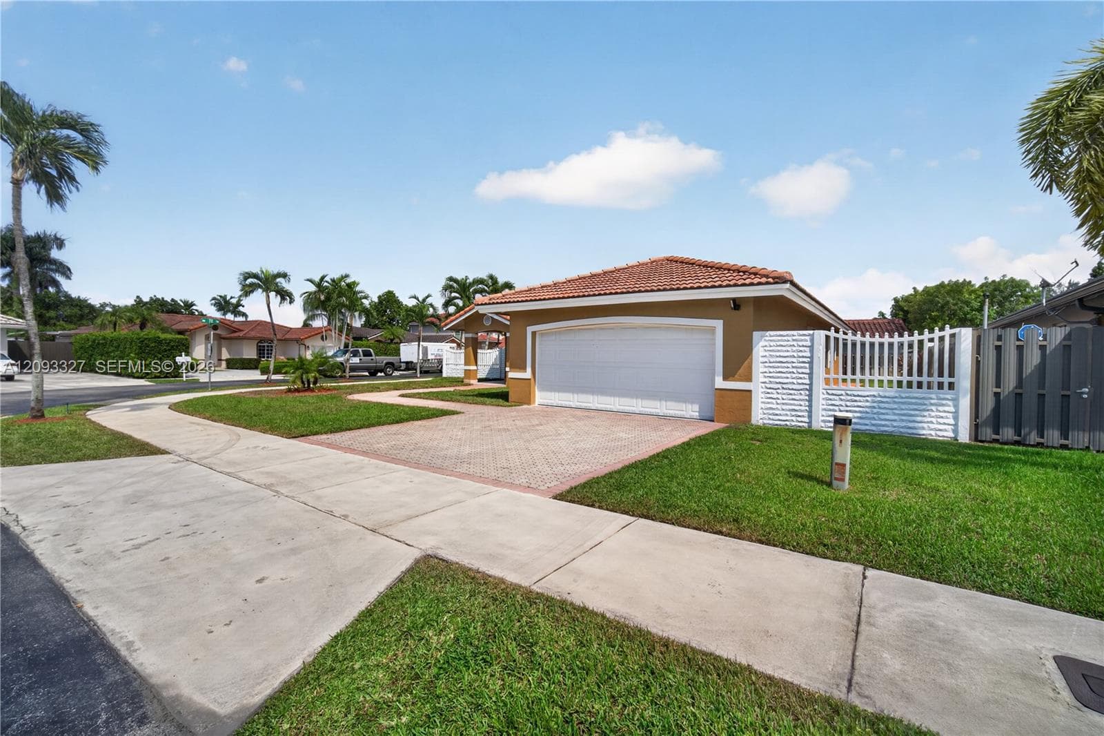 Exterior elevation featuring a tile roof, paver driveway, two-car garage, and white perimeter fencing