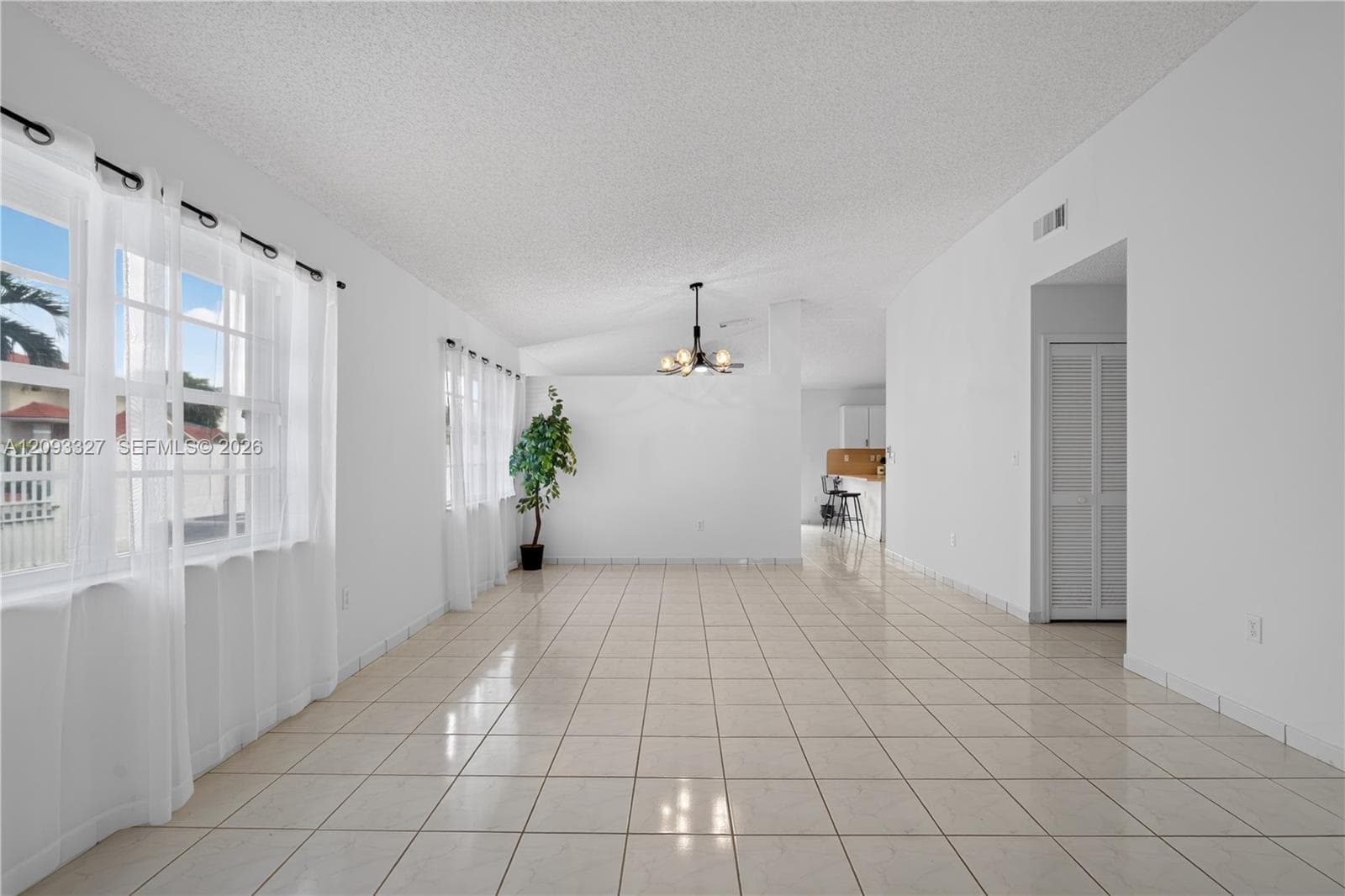 Open-concept living space featuring large-format ceramic tile flooring, multi-pane windows, a multi-arm chandelier, and louvered bifold closet doors