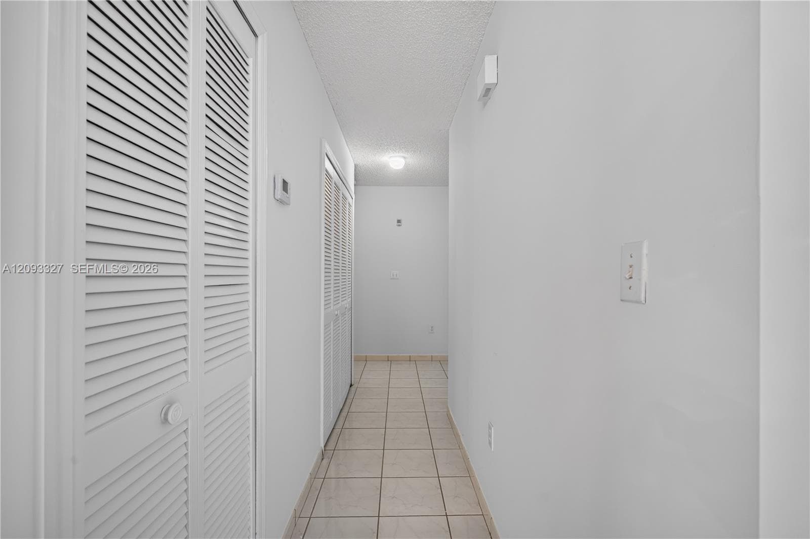 Hallway featuring neutral-tone tile flooring and dual louvered-style closet doors