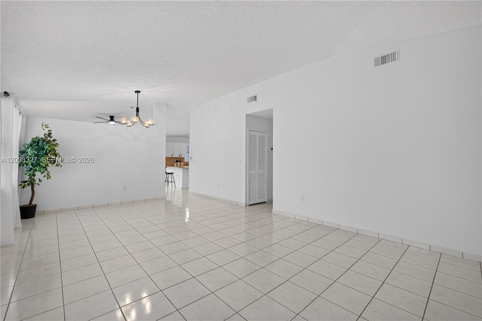 Open floor plan featuring large-format ceramic tile flooring, a multi-arm chandelier, and louvered-panel closet doors