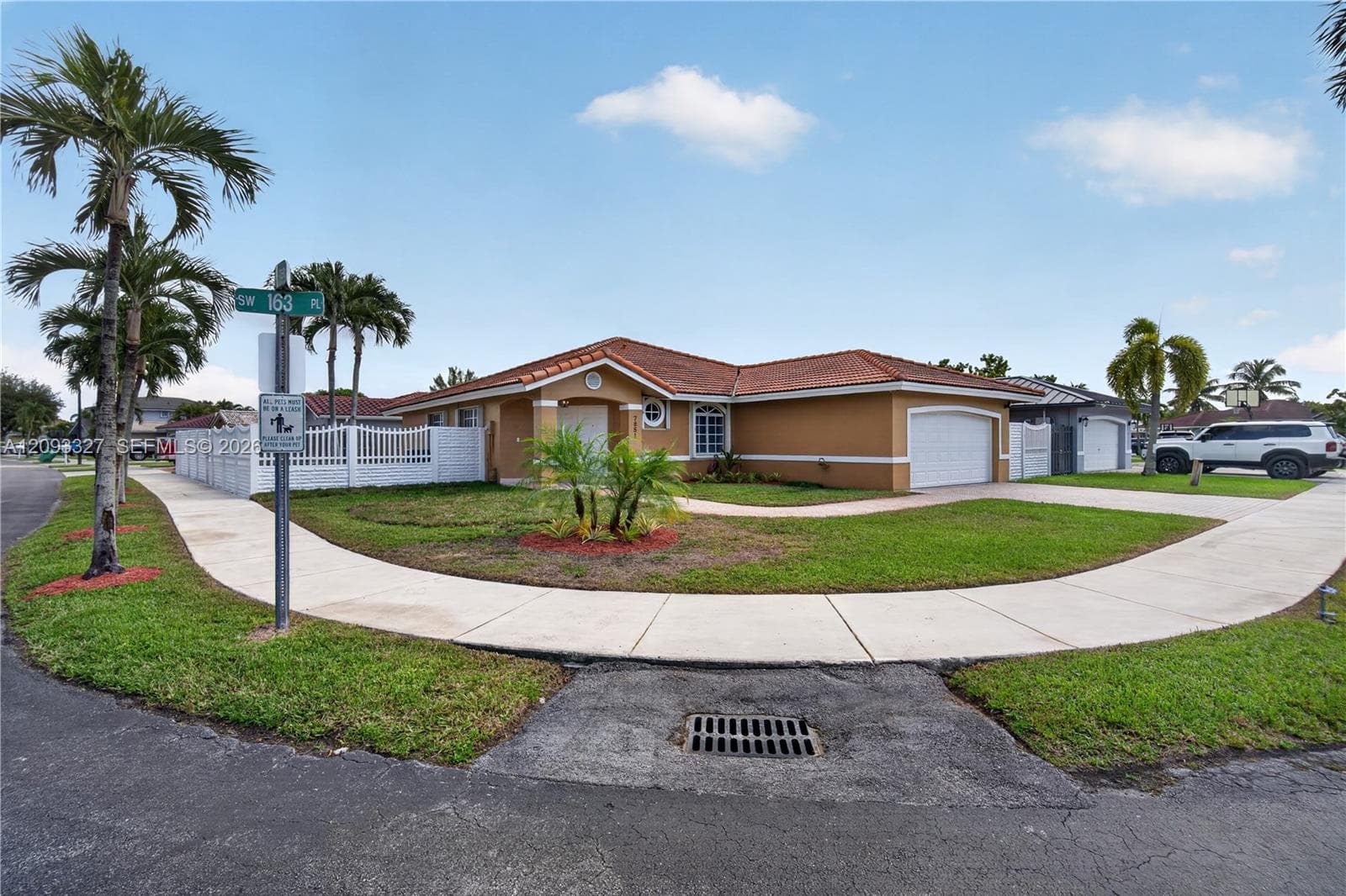 Single-story residence featuring a tile roof, stucco exterior, two-car garage, white vinyl perimeter fencing, and mature palm trees