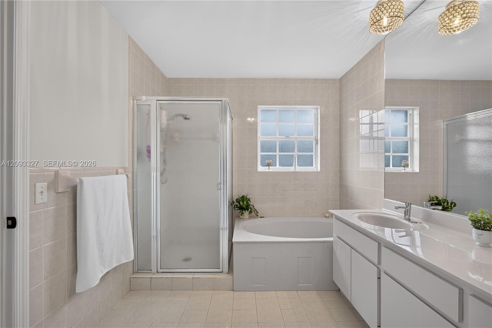 Bathroom featuring a recessed soaking tub, a glass-enclosed shower, a double-basin vanity with a solid-surface countertop, and full-wall ceramic tile surround