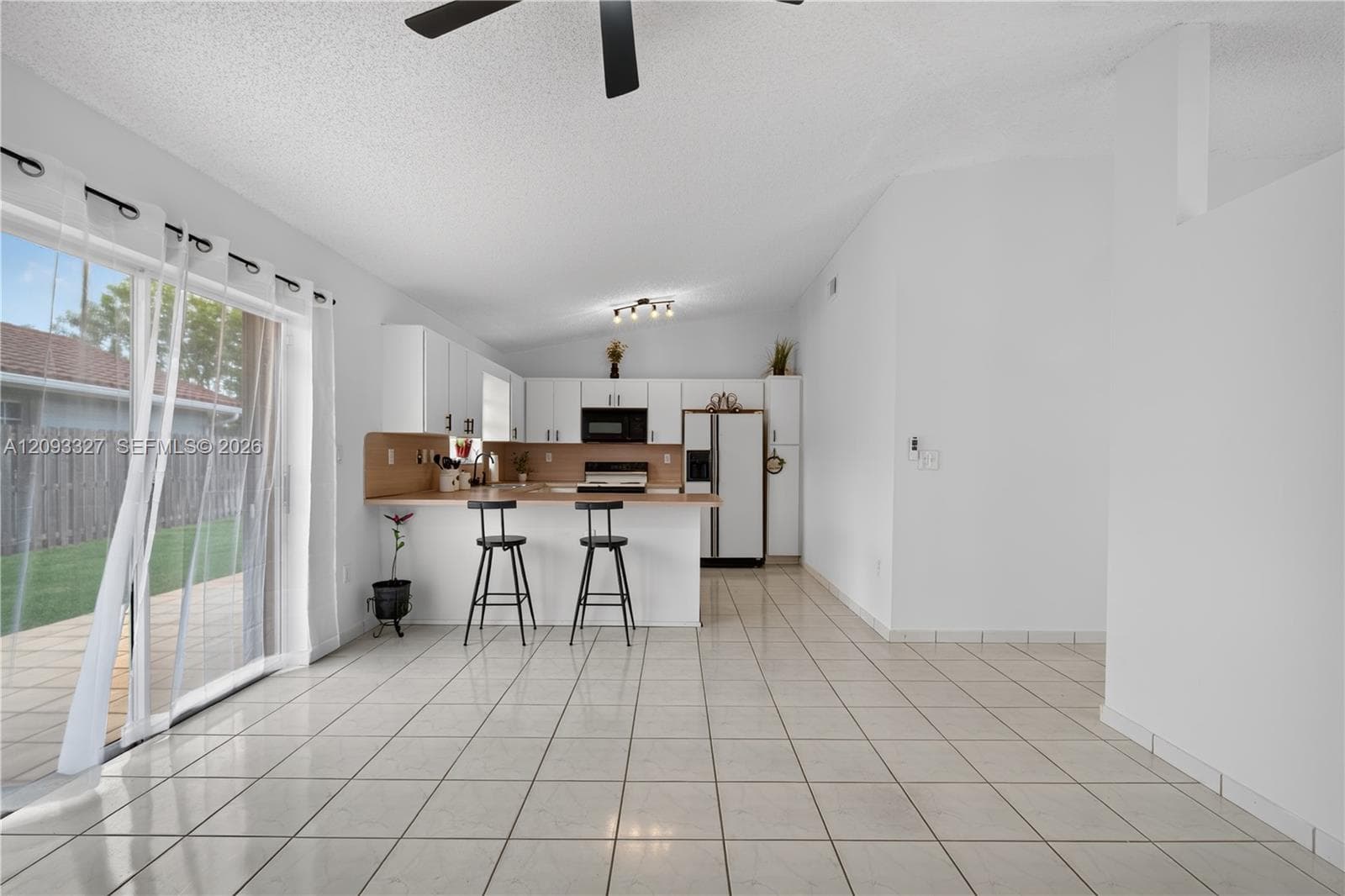 Open-concept kitchen featuring white cabinetry, neutral countertops, a breakfast bar, and tile flooring, with sliding glass doors providing outdoor access