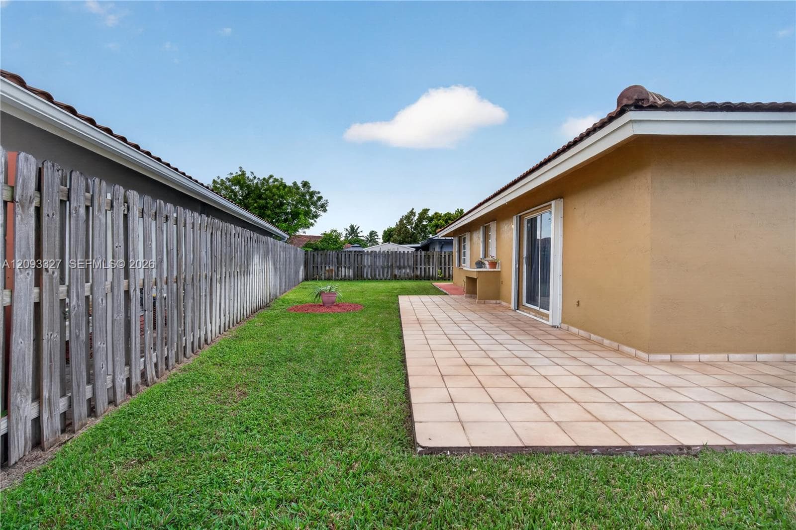 Rear exterior featuring a tiled patio, stucco siding, a built-in outdoor counter, and a fenced yard with a grass lawn