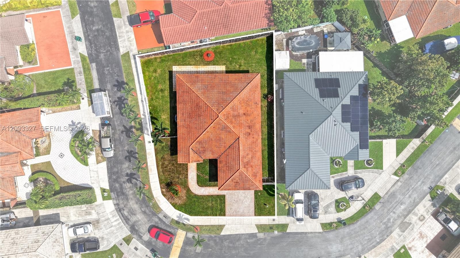 Aerial perspective of a corner lot property featuring a clay tile roof, paved walkway, and manicured lawn