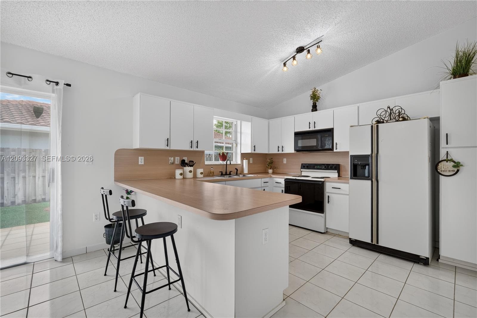 Kitchen featuring white cabinetry, a wood-finish countertop breakfast bar, tile flooring, track lighting, and a sliding glass door