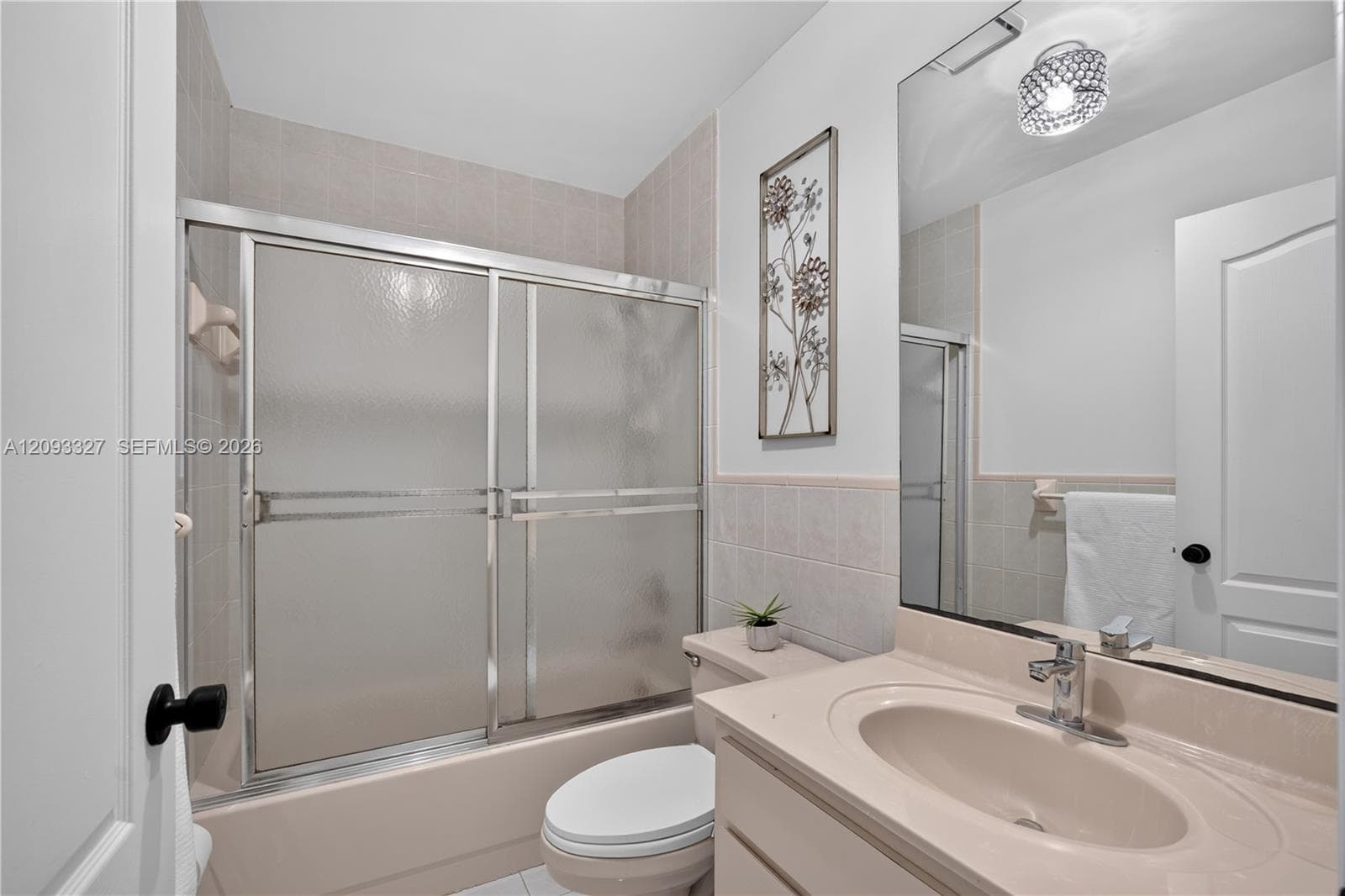 Bathroom featuring a vanity with integrated sink, chrome faucet, wall-to-wall mirror, textured glass sliding shower door, and tile surround