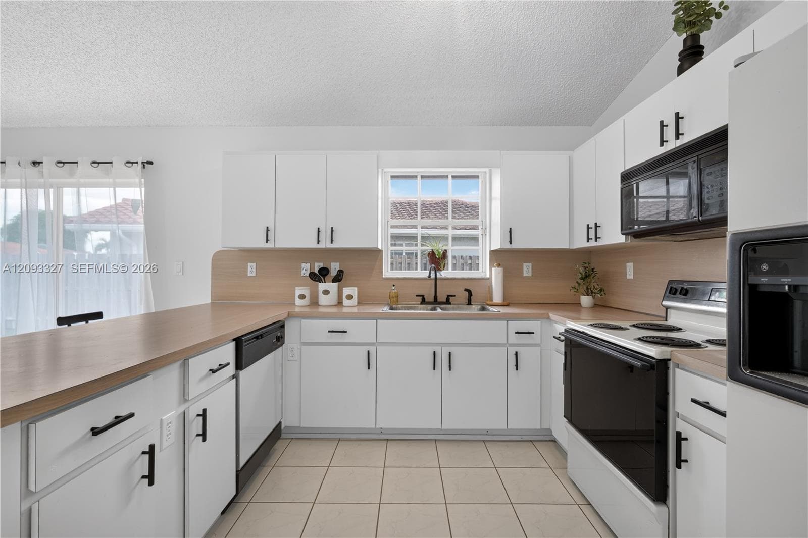 Kitchen featuring white cabinetry with matte black hardware, light-toned countertops, a tile backsplash, and ceramic tile flooring