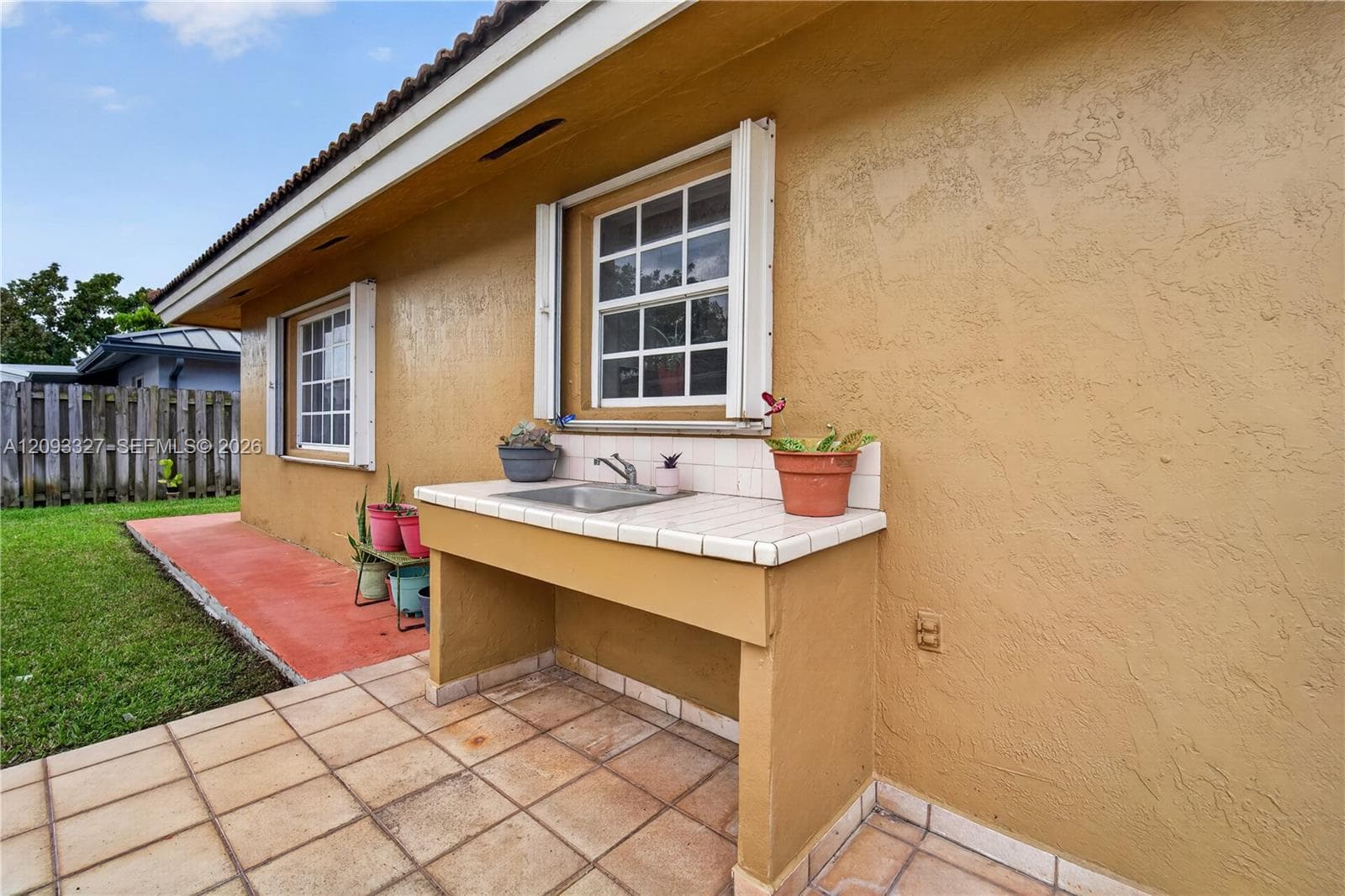 Exterior sink station featuring a tile countertop, integrated basin, and metal faucet, set on a tiled patio