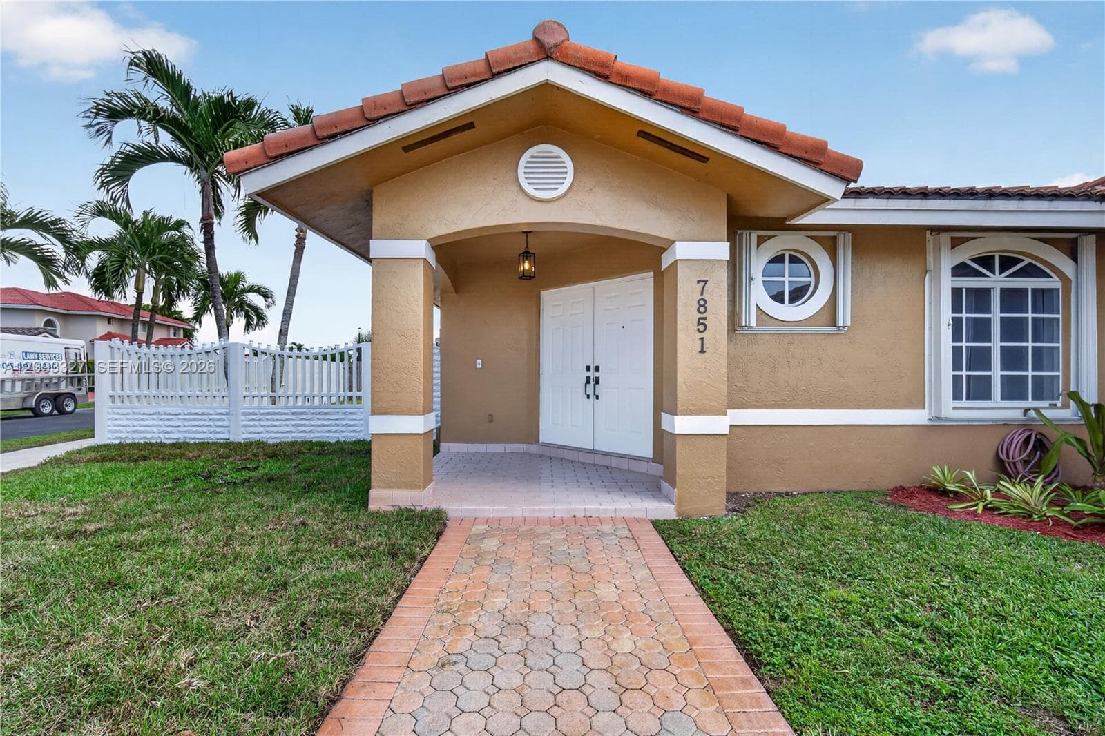 Stucco exterior featuring a tiled gable roof, covered entryway, arched windows, and a paved walkway