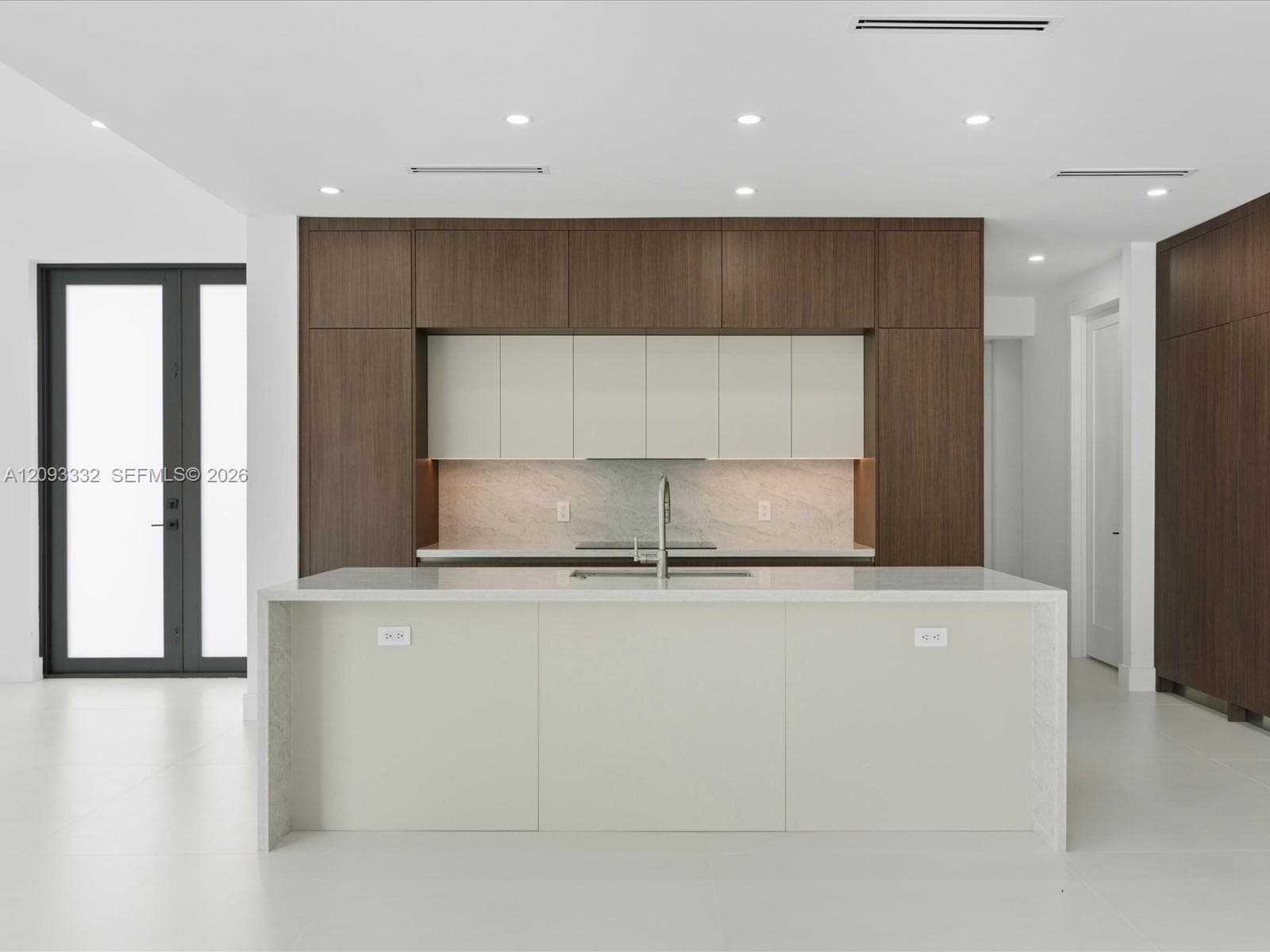 Contemporary kitchen featuring two-toned cabinetry, a waterfall-edge center island, solid-surface countertops, stone-finish backsplash, and recessed ceiling lighting