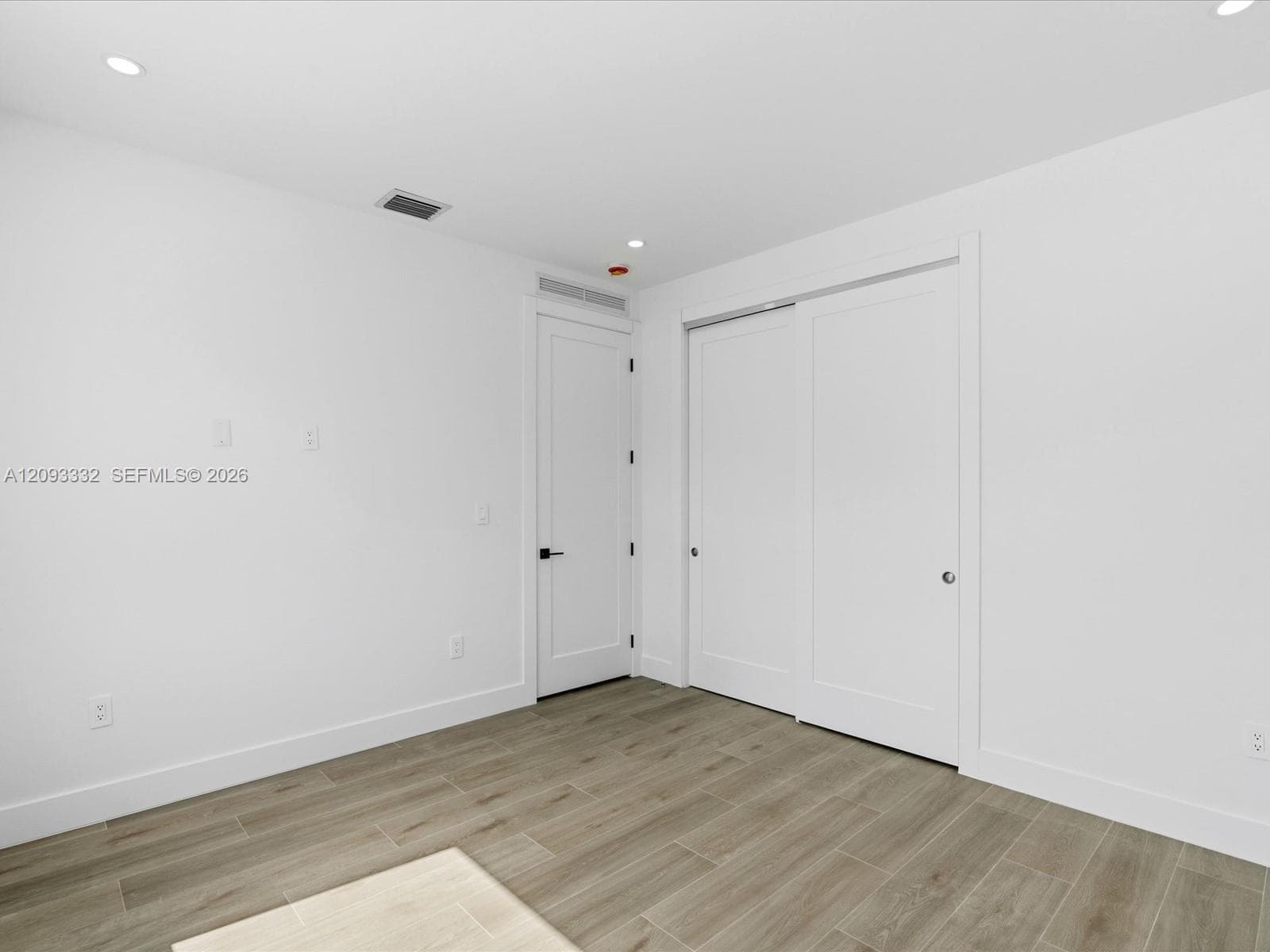 Neutral-toned wood-finish tile flooring, recessed ceiling lighting, and sliding closet doors with matte black hardware