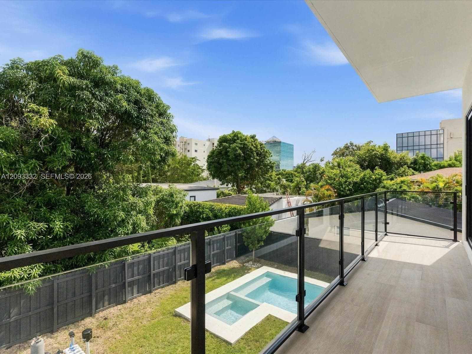 Balcony featuring light-toned tile flooring and a glass railing with a dark metal frame, overlooking a rear yard with an in-ground swimming pool and perimeter fencing