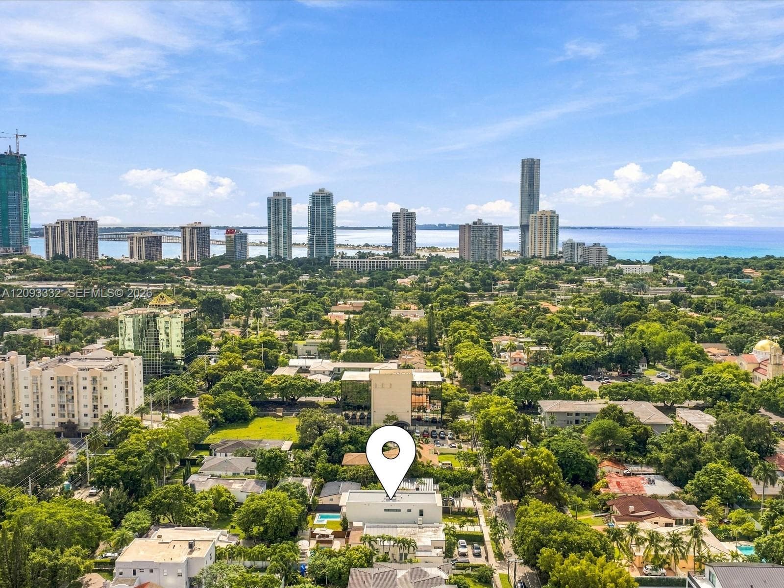 Aerial perspective featuring a residential lot with a swimming pool, mature canopy trees, and high-rise urban skyline scenery
