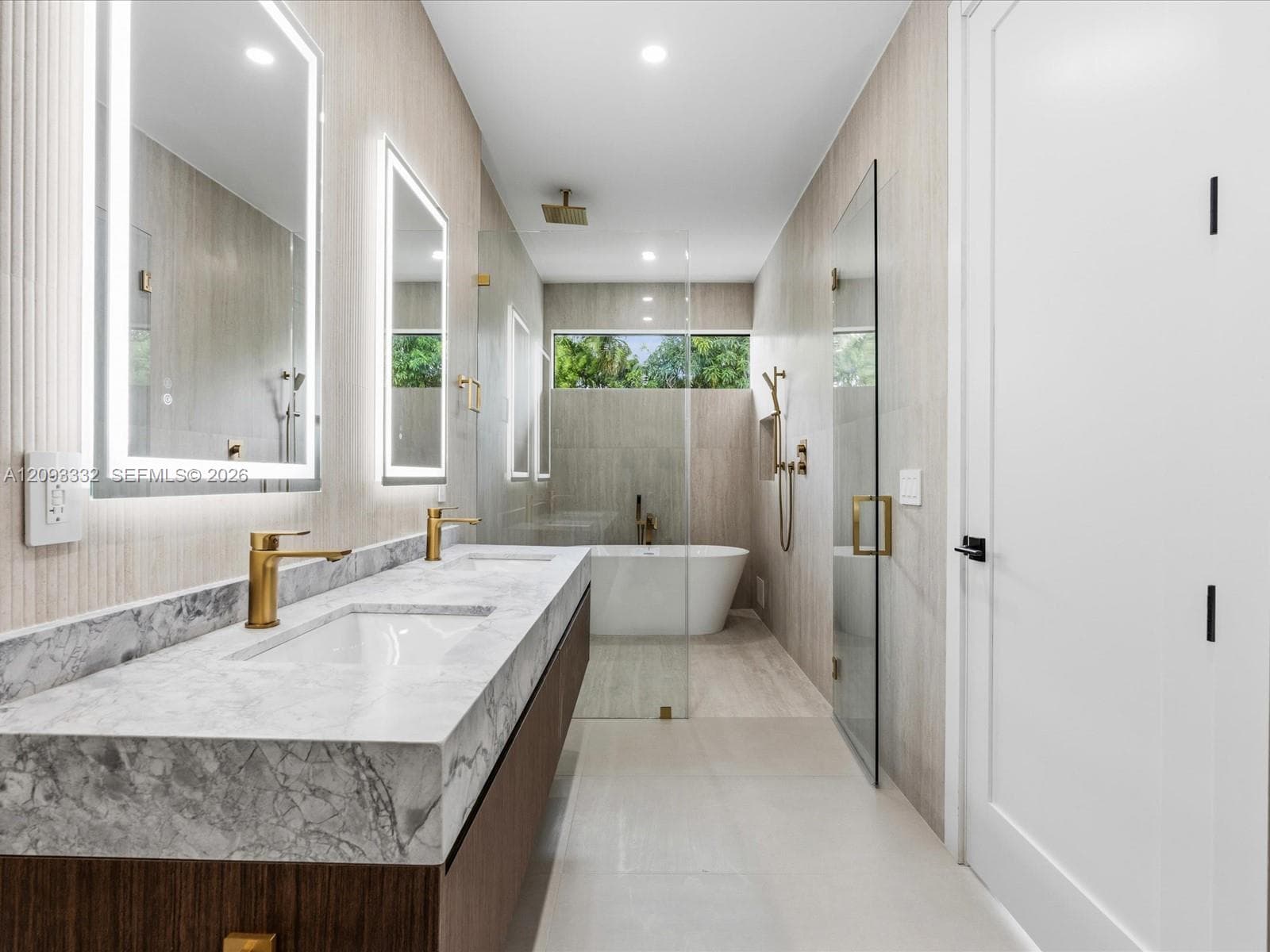 Dual-sink vanity with stone countertop and integrated lighting, walk-in glass shower enclosure, freestanding soaking tub, and metallic gold-finish fixtures